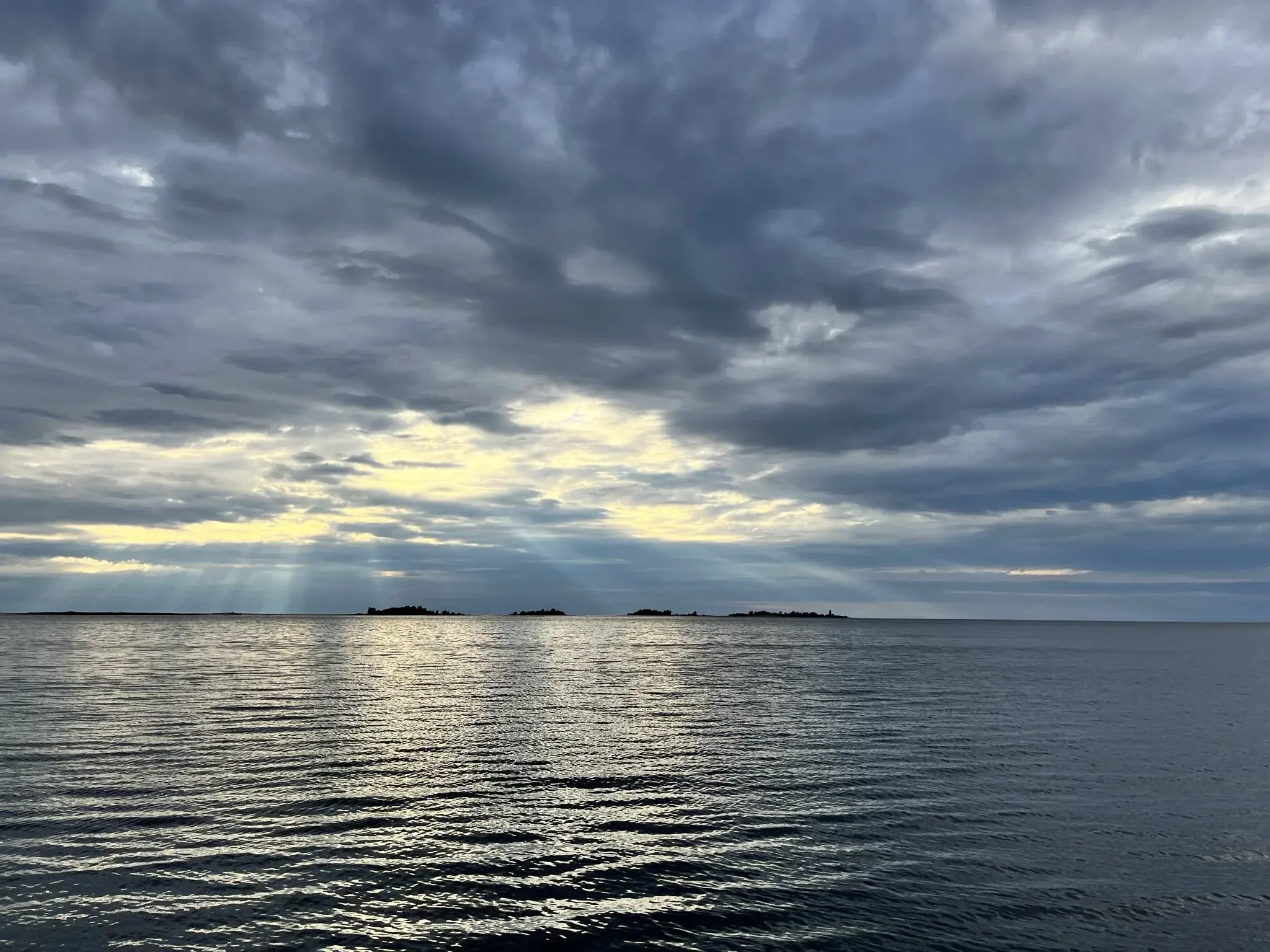 Cloudy skies over a serene sea with small islands in the background bathing in light pillars. Picture taken in front of the town of Raahe on a boat. More detailed location between Preiskari and Tasku islands
